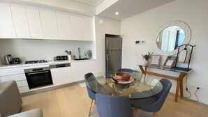 A modern kitchen with white cabinets, a built-in oven, and a dining area with a glass table and two chairs. - Executive Oasis | Chic 1BR + Courtyard Retreat (Engadine)