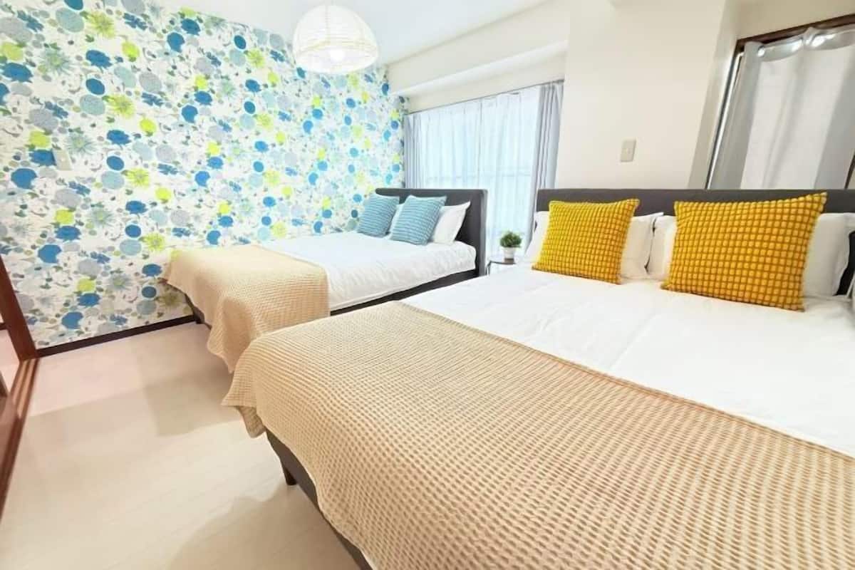A hotel room with two beds, a patterned wall, a window with curtains, and a hanging light fixture.