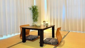 A traditional Japanese-style room with tatami flooring, a low wooden table, two cushioned chairs, a potted plant, and a lamp. - City Heim Building (Tokyo)