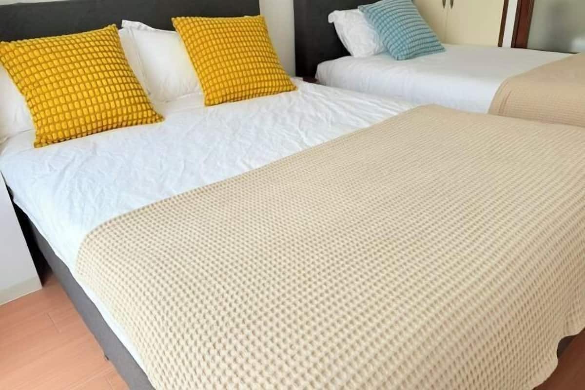 A hotel room with two beds, each with white bedding and different patterned pillows.