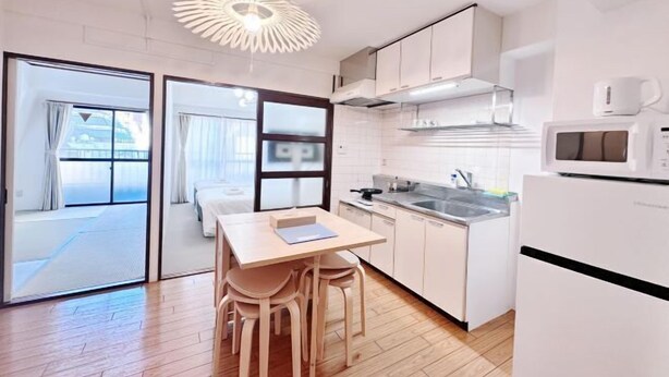A modern kitchen with white cabinets, a wooden dining table, and a unique ceiling light fixture. - City Heim Building (Tokyo)
