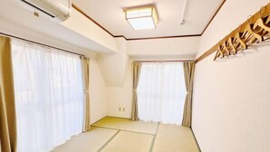 A room with tatami flooring, two windows with sheer curtains, a ceiling fan, and a wooden coat rack. - City Heim Building (Tokyo)