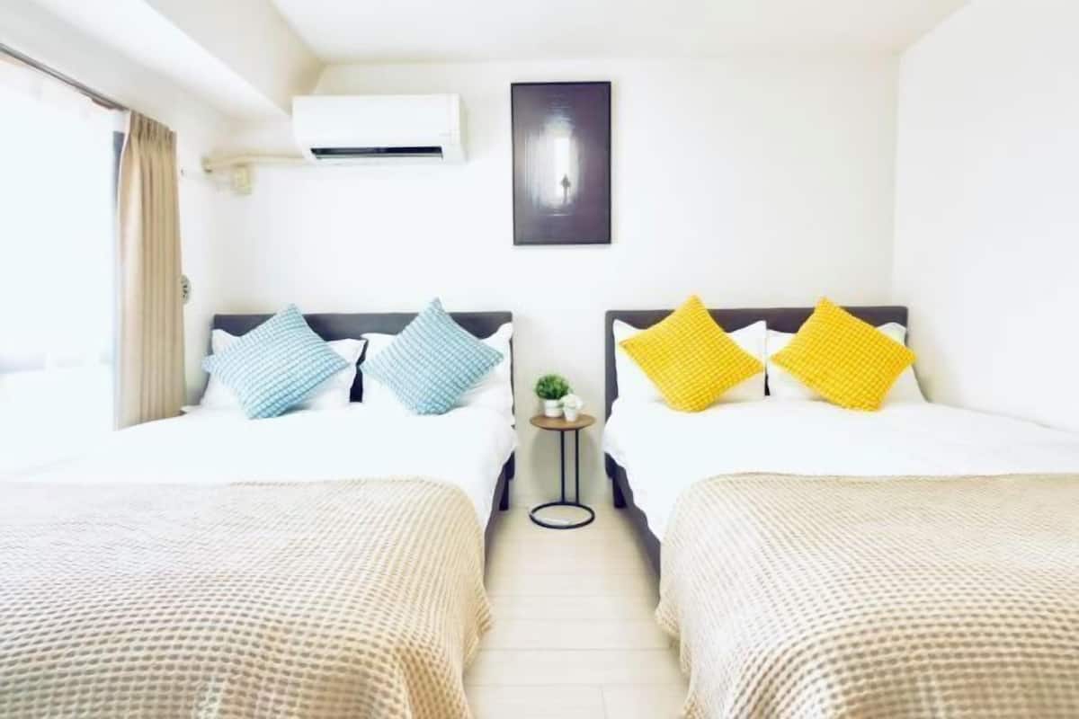 A hotel room with two beds, a small table with a plant, and a wall-mounted air conditioner.