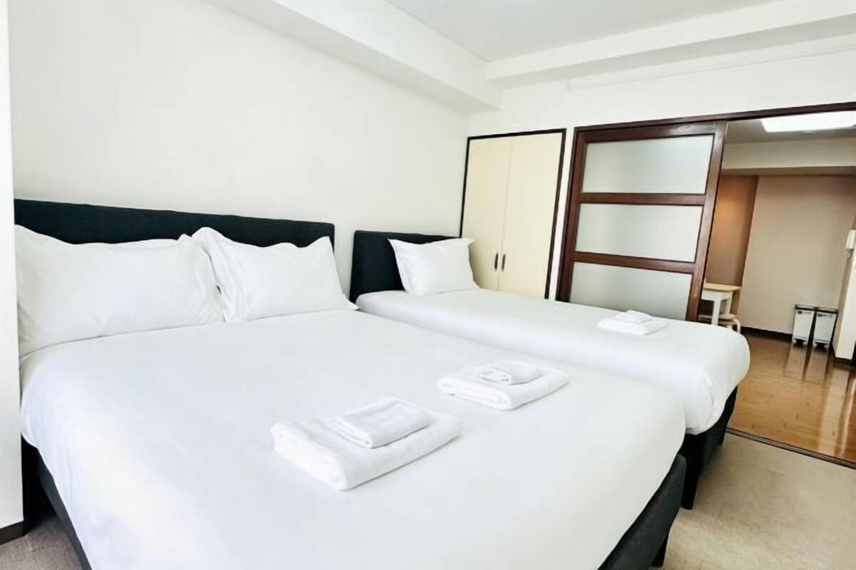 A hotel room with two beds, white linens, and a wooden wardrobe.