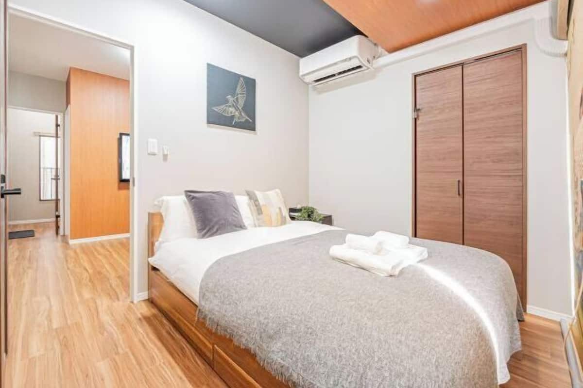 A bedroom with a bed, a wooden wardrobe, and a wall-mounted air conditioner.