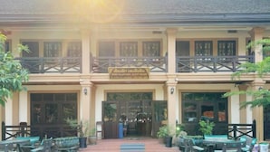 A building with a sign indicating it is a guest house. There are outdoor tables and chairs, and the entrance has a glass door. - Nan Ya Hotel(Sene Hua Phanh Guesthouse) (Luang Prabang)