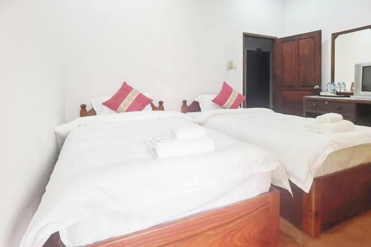 A hotel room with two beds, wooden headboards, white bedding, and a wooden dresser with a mirror.