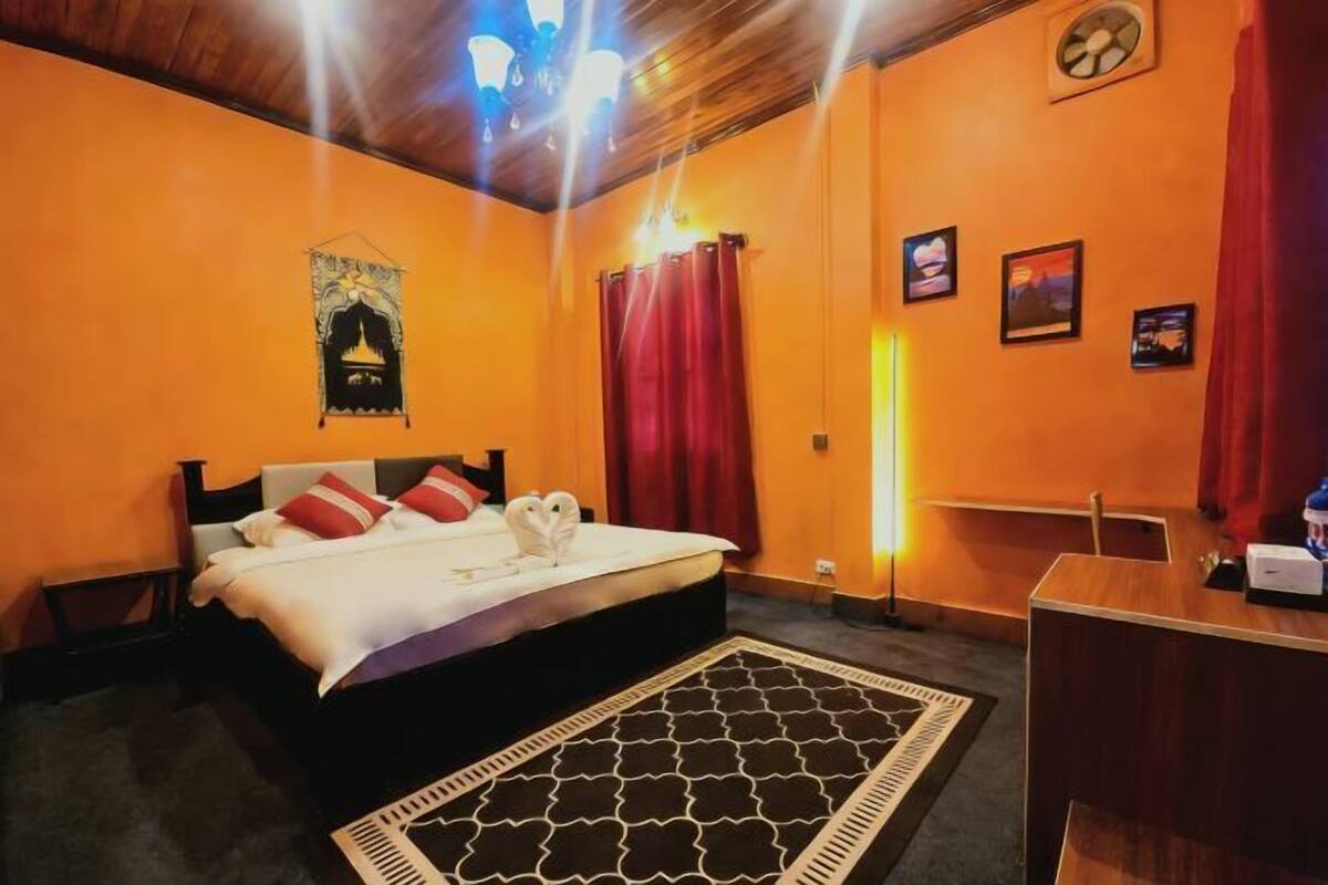 A hotel room with a bed, a desk, a wall clock, and a wall-mounted tapestry.