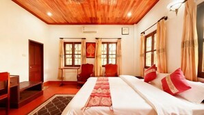 A hotel room with a wooden ceiling, a bed with red and white bedding, two chairs, a desk, and a window with curtains. - Nan Ya Hotel(Sene Hua Phanh Guesthouse) (Luang Prabang)