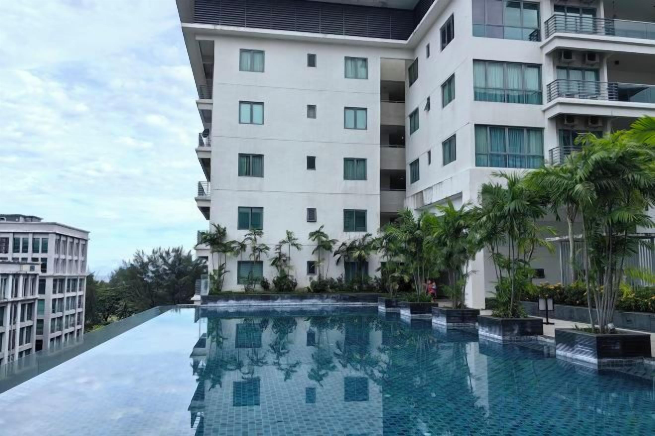 A modern hotel with a rooftop infinity pool, surrounded by lush greenery and adjacent buildings.