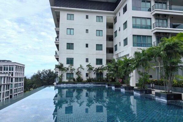 Un hôtel moderne doté d’une piscine à débordement sur le toit, entouré d’une végétation luxuriante et bordé d’immeubles.