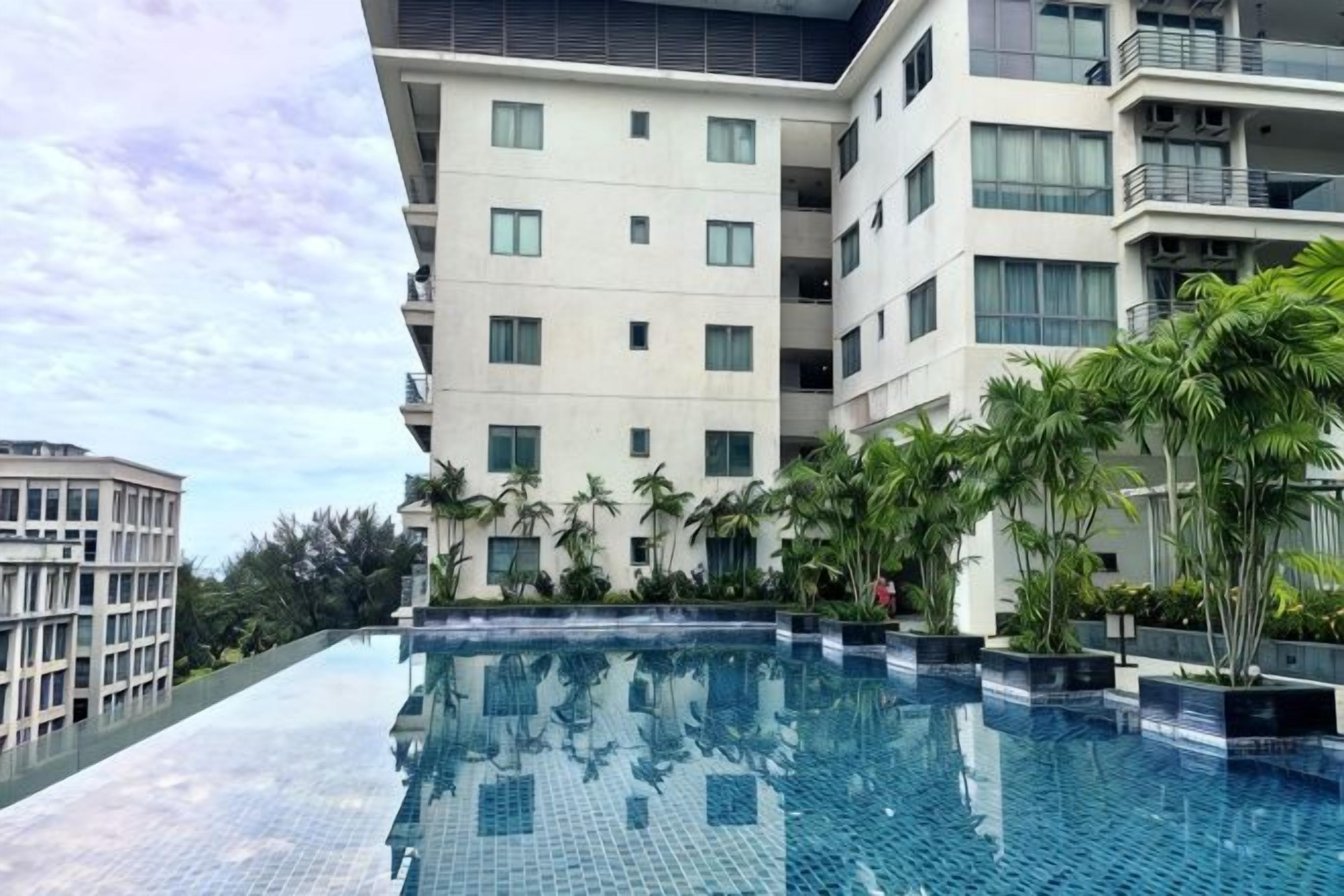 A modern hotel with a rooftop infinity pool, surrounded by palm trees and a clear sky.