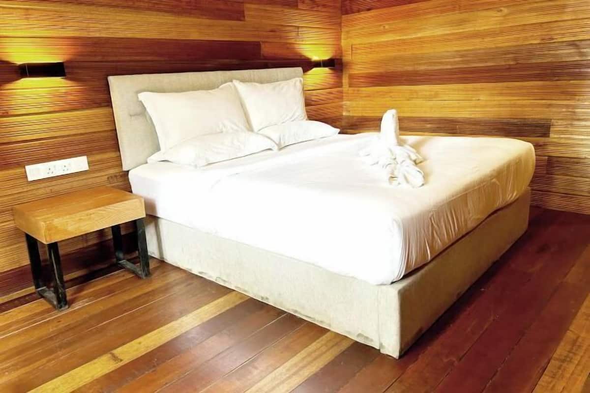 A neatly made bed with a wooden headboard and a bedside table in a room with wooden panel walls and flooring.