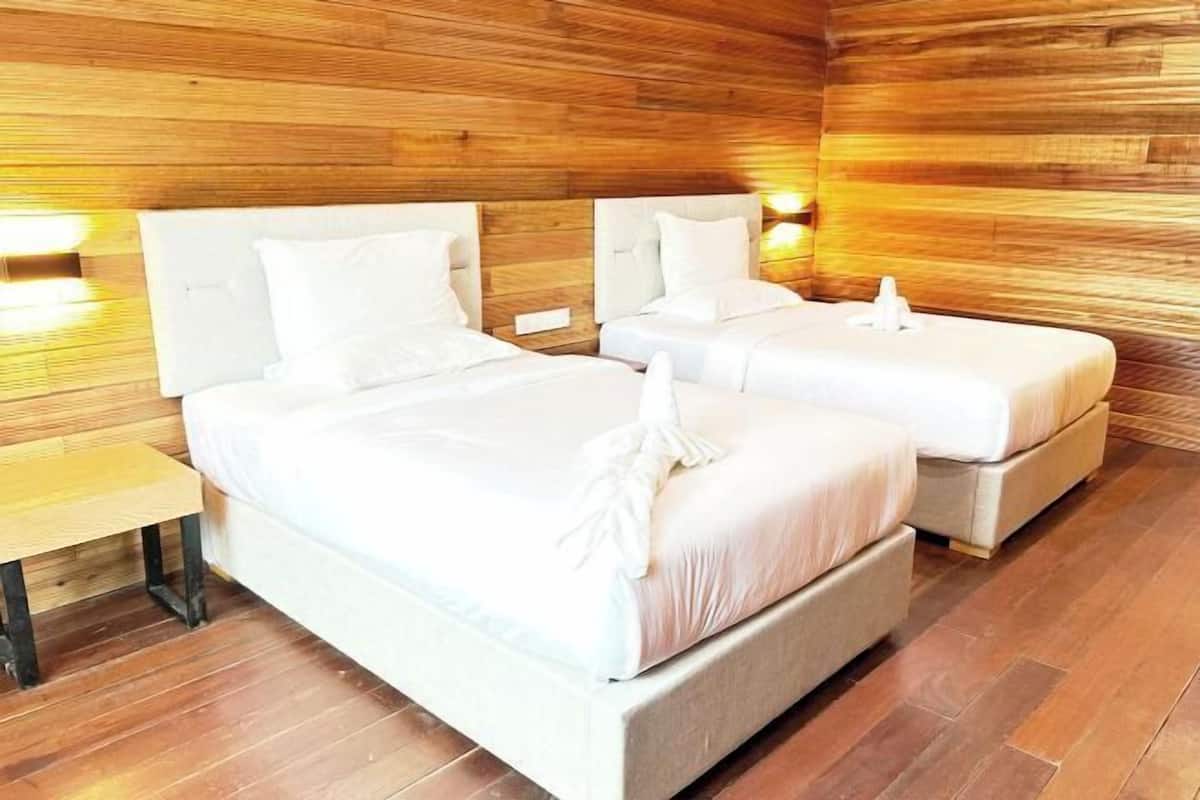 A wooden-paneled room with two beds, each with white bedding and headboards, and a small wooden table.