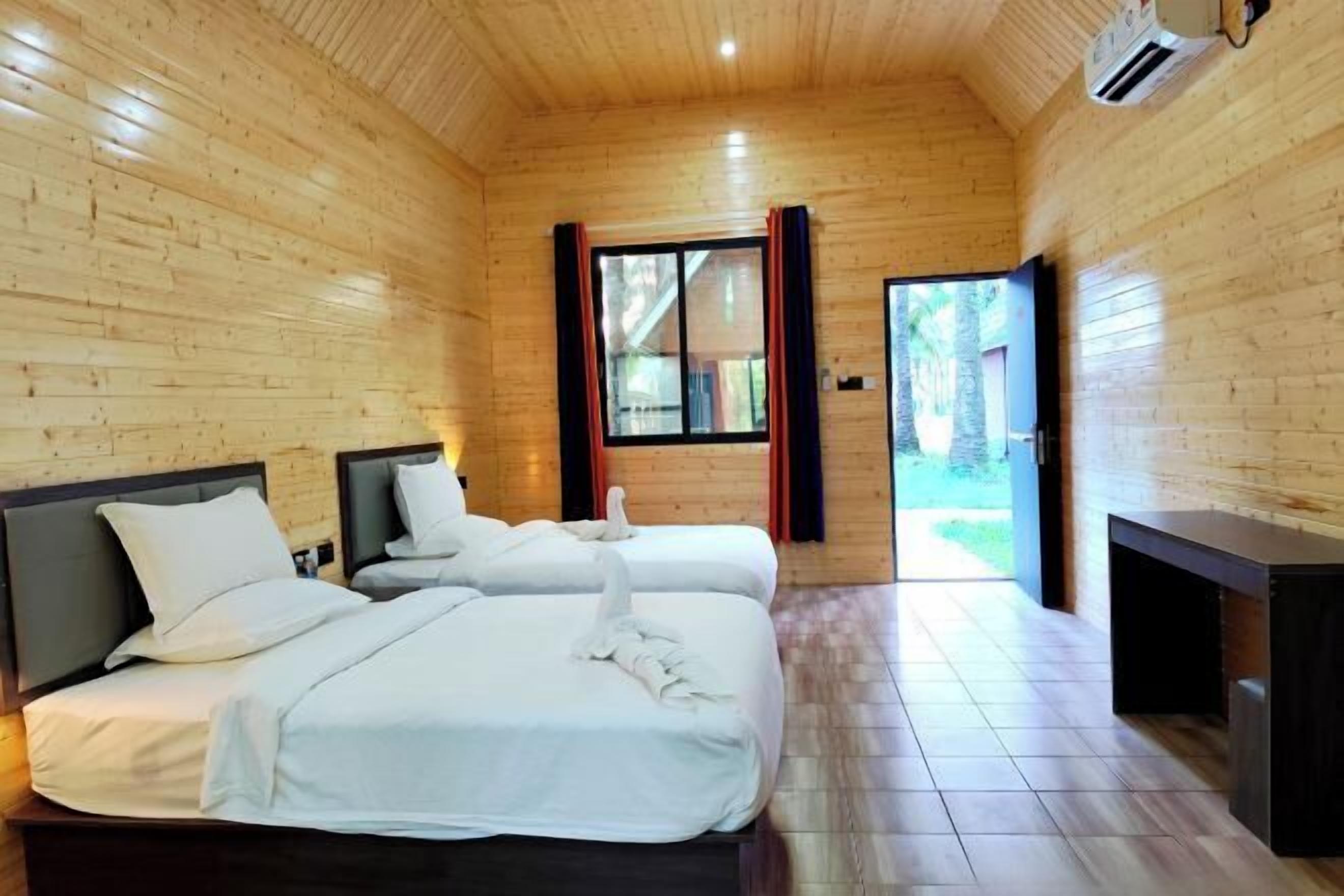 A wooden cabin room with two beds, a bench, and a large window.