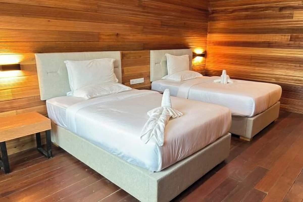 A room with two beds, wooden walls, and a bench.