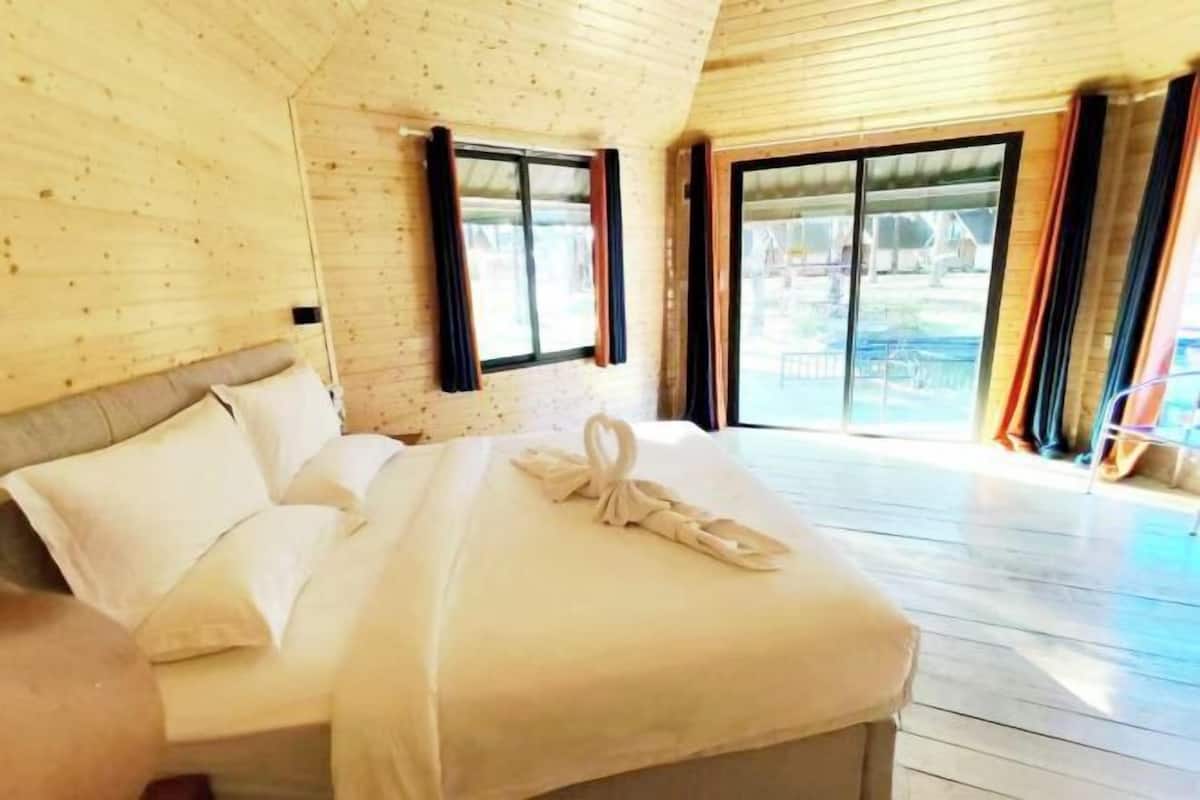 A wooden-paneled room with a bed, large windows, and a view of the outdoors.