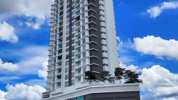 A tall residential building with multiple balconies, a clear sky, and a few trees.