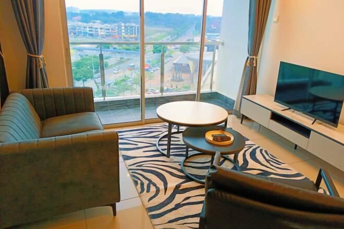 Ein modernes Wohnzimmer mit einer Couch, einem runden Couchtisch, einem Flachbildfernseher und einem großen Fenster mit Blick auf die Stadt.