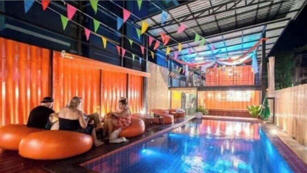 Una piscina interna con bandierine triangolari colorate, pannelli in legno e zone relax arancioni.