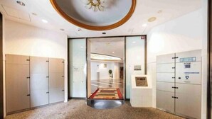 Un moderno vestíbulo de hotel con una zona central alfombrada que conduce a una recepción, puertas de cristal y un techo con iluminación empotrada.