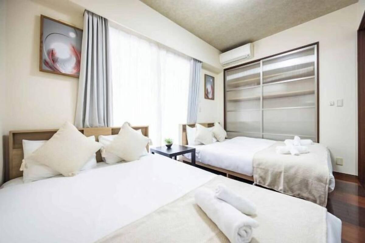 Quarto de hotel com duas camas, uma janela grande com cortinas, ar-condicionado fixado na parede e uma porta de vidro deslizante.