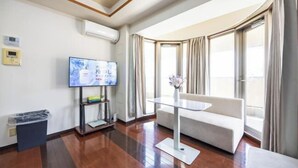Habitación de hotel con televisor de pantalla plana, sofá, una mesita y ventana con cortinas.