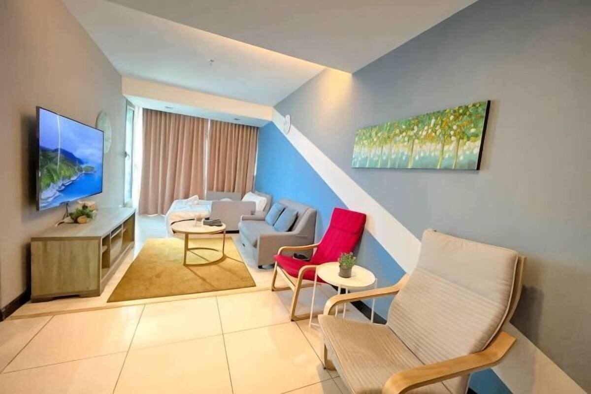 A modern living room with a flat-screen TV, a sofa, a red chair, a white armchair, and a painting on the wall.