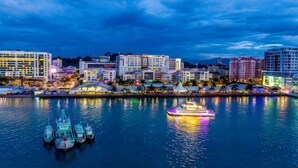 A waterfront cityscape with buildings, a marina with boats, and a river reflecting the city lights. - Urban Retreat @ KK Sky • Pool • Parking (Kota Kinabalu)