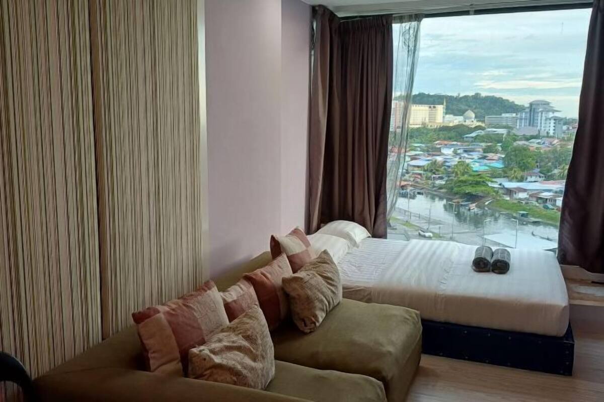 A room with a large window, a sofa, a bed, and a view of a cityscape.