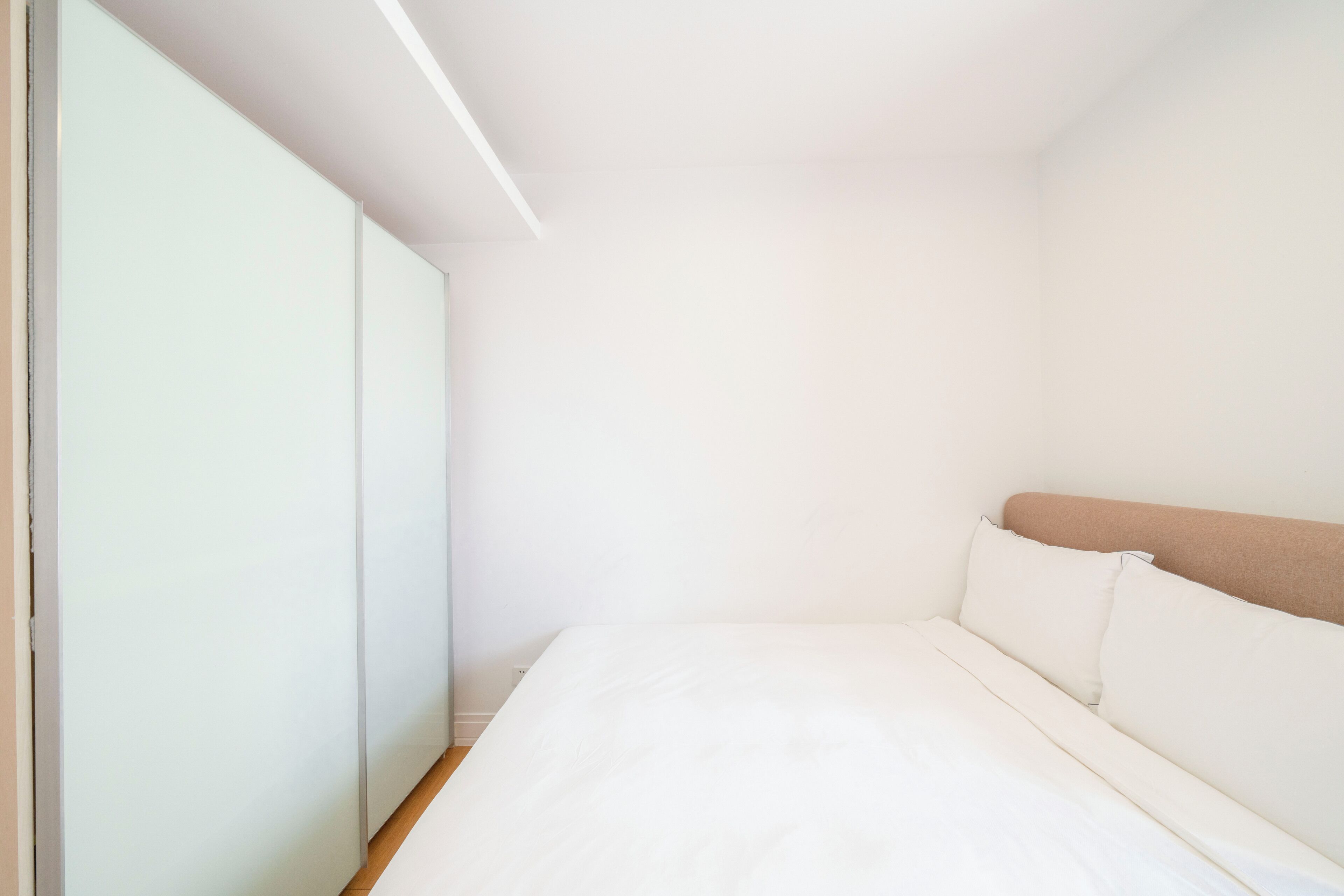 Un dormitorio con cama, paredes blancas y suelo de madera.