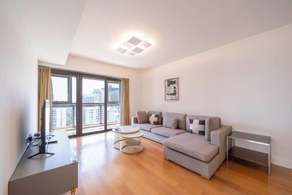 A modern living room with a sectional sofa, a small round table, and a TV on a desk.