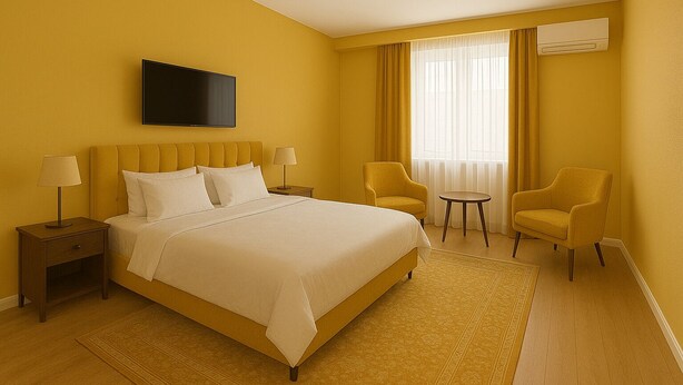 A hotel room with a large bed, two bedside tables with lamps, a TV mounted on the wall, two armchairs, and a small round table.