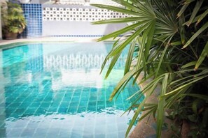Una piscina azul cristalina con borde de azulejos y una planta en primer plano.