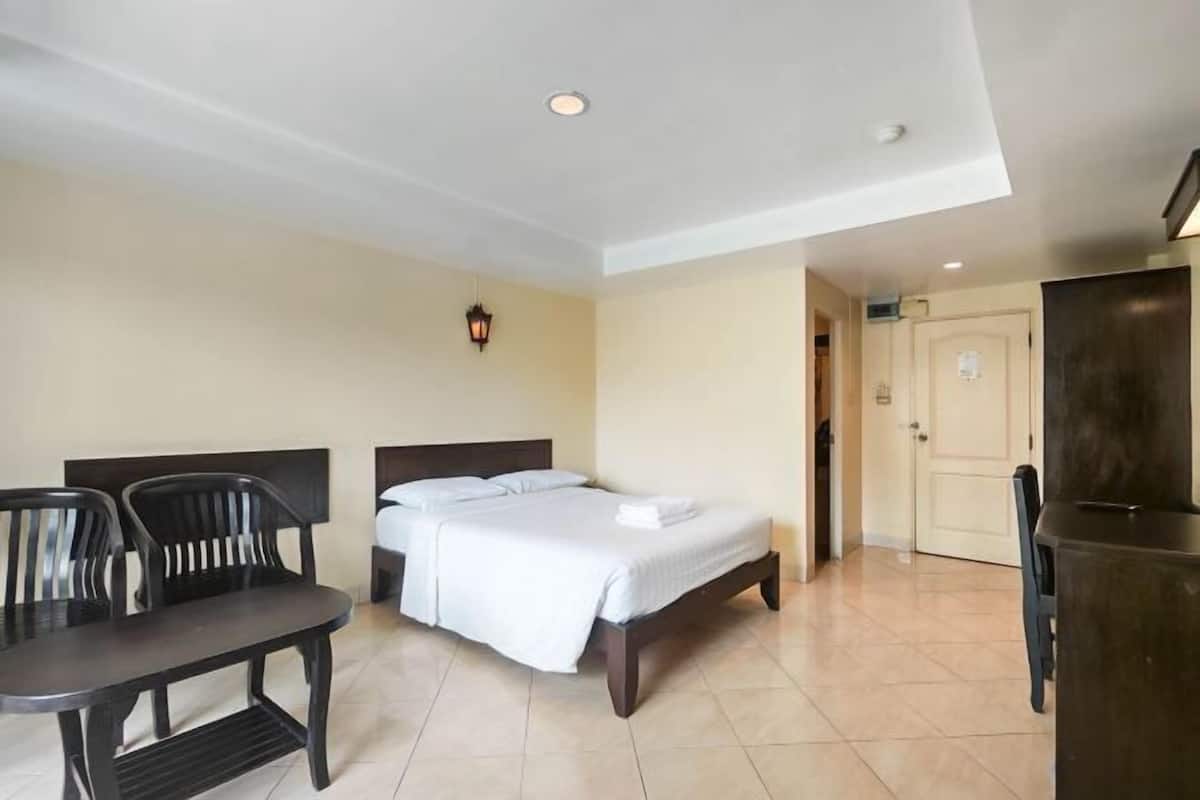 A hotel room with a bed, a desk, two chairs, a lamp, and a door.