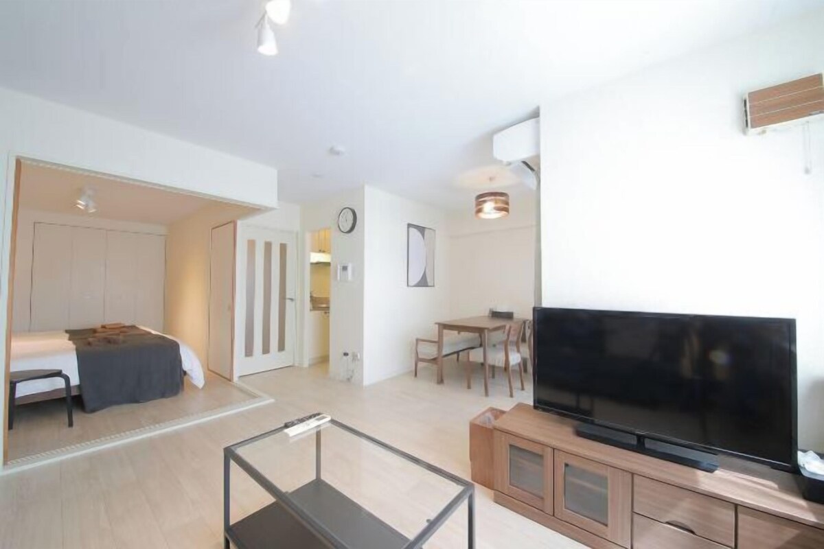Una sala moderna con televisión de pantalla plana, comedor y habitación con cama y escritorio.