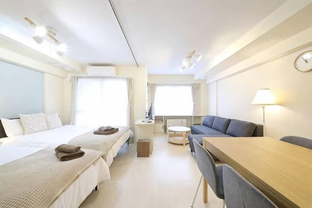 A modern hotel room with two beds, a dining table, a sofa, and a small desk.