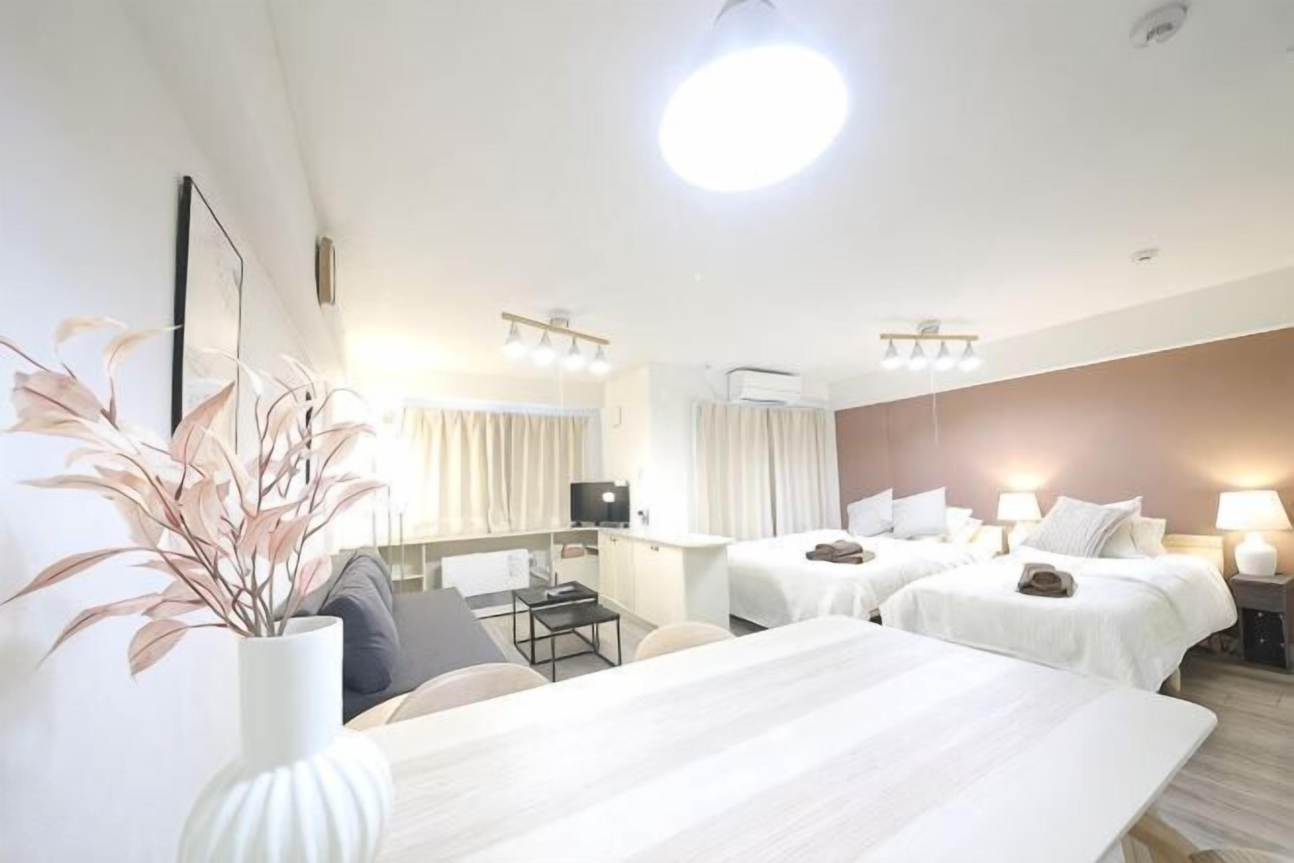 Una habitación de hotel con cama, mesitas de noche, escritorio, silla, televisor y una planta.