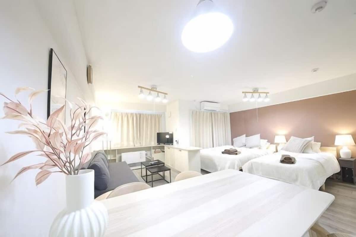 Una habitación de hotel con cama, mesitas de noche, escritorio, silla, televisor y una planta.