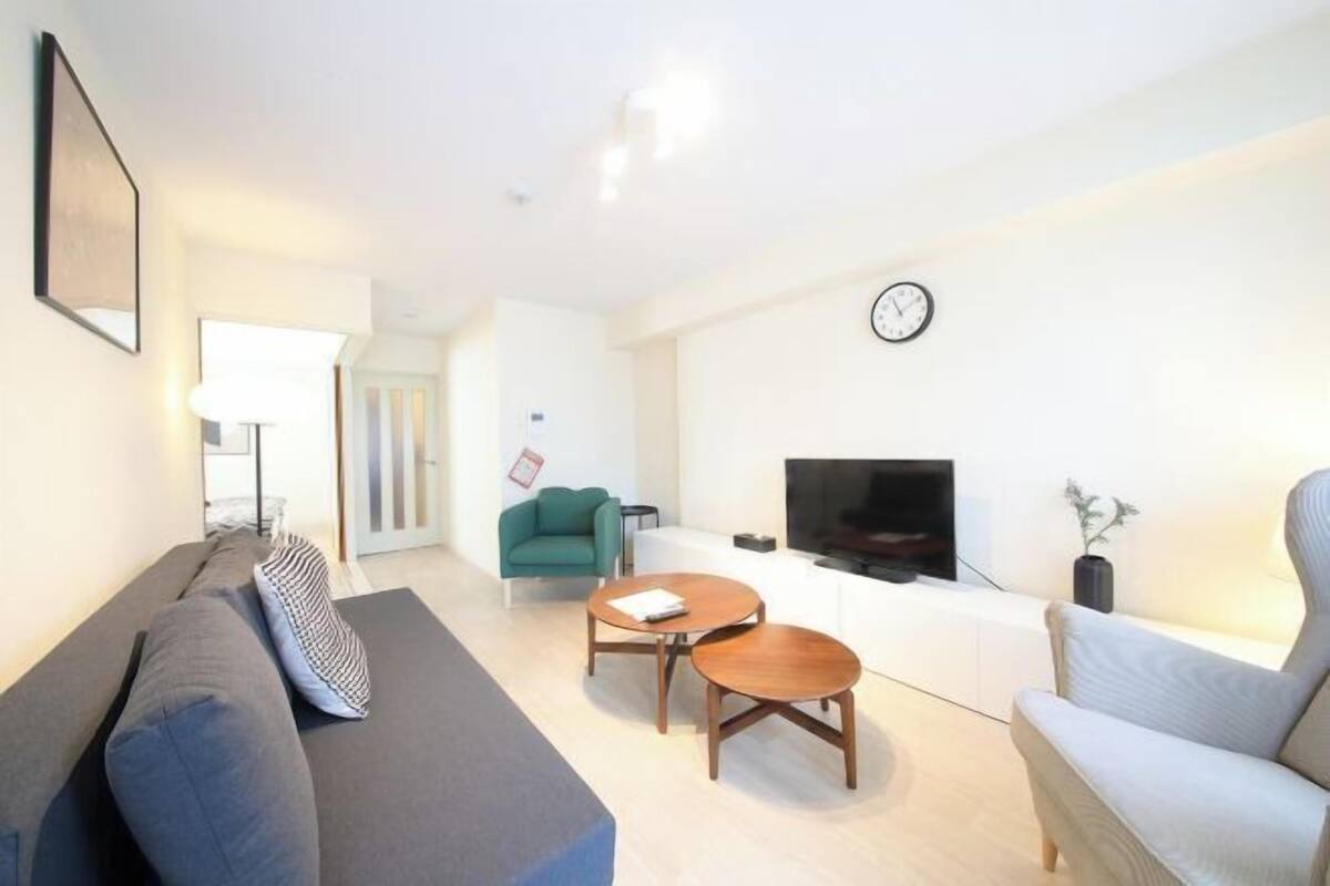 A modern living room with a sofa, two coffee tables, a TV, and a clock on the wall.
