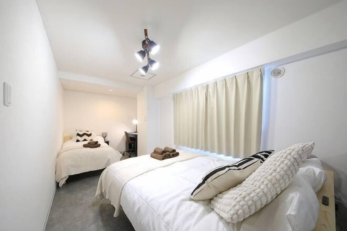 A hotel room with two beds, a desk, a chair, and a window with curtains.