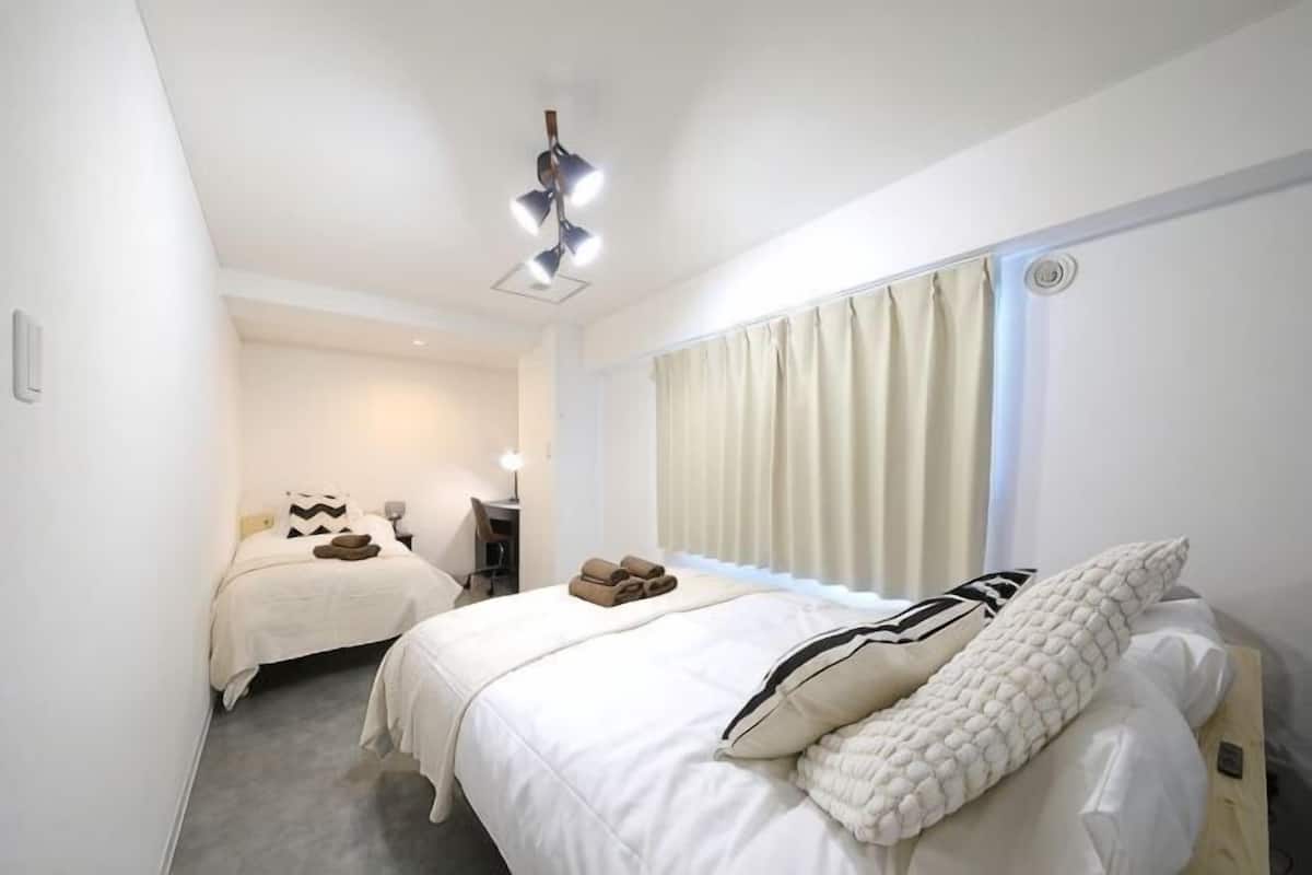 Habitación de hotel con dos camas, un escritorio, una silla y una ventana con cortinas.