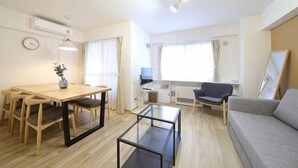 A modern living room with a sofa, a dining table with chairs, a coffee table, and a TV. - Northern Hills Minami 6 (Sapporo)