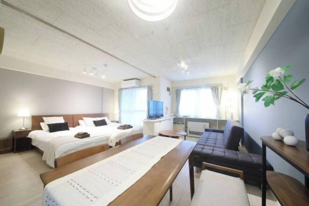 A hotel room with two beds, a desk, a sofa, a TV, and a large window.