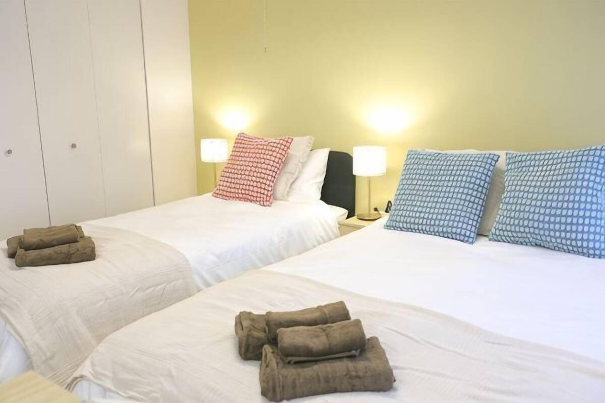 Two beds with white linens, brown towels, and bedside lamps.