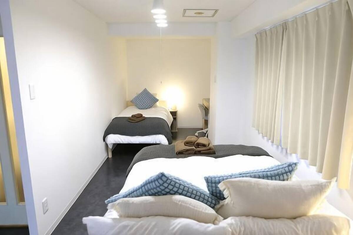 A hotel room with two beds, a nightstand, a lamp, and a window with curtains.