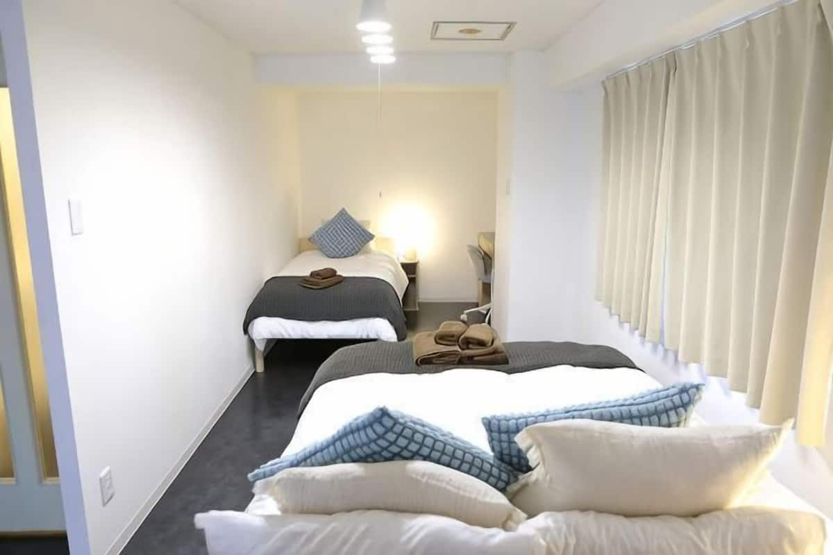 Habitación de hotel con dos camas, una mesita de noche, una lámpara y una ventana con cortinas.