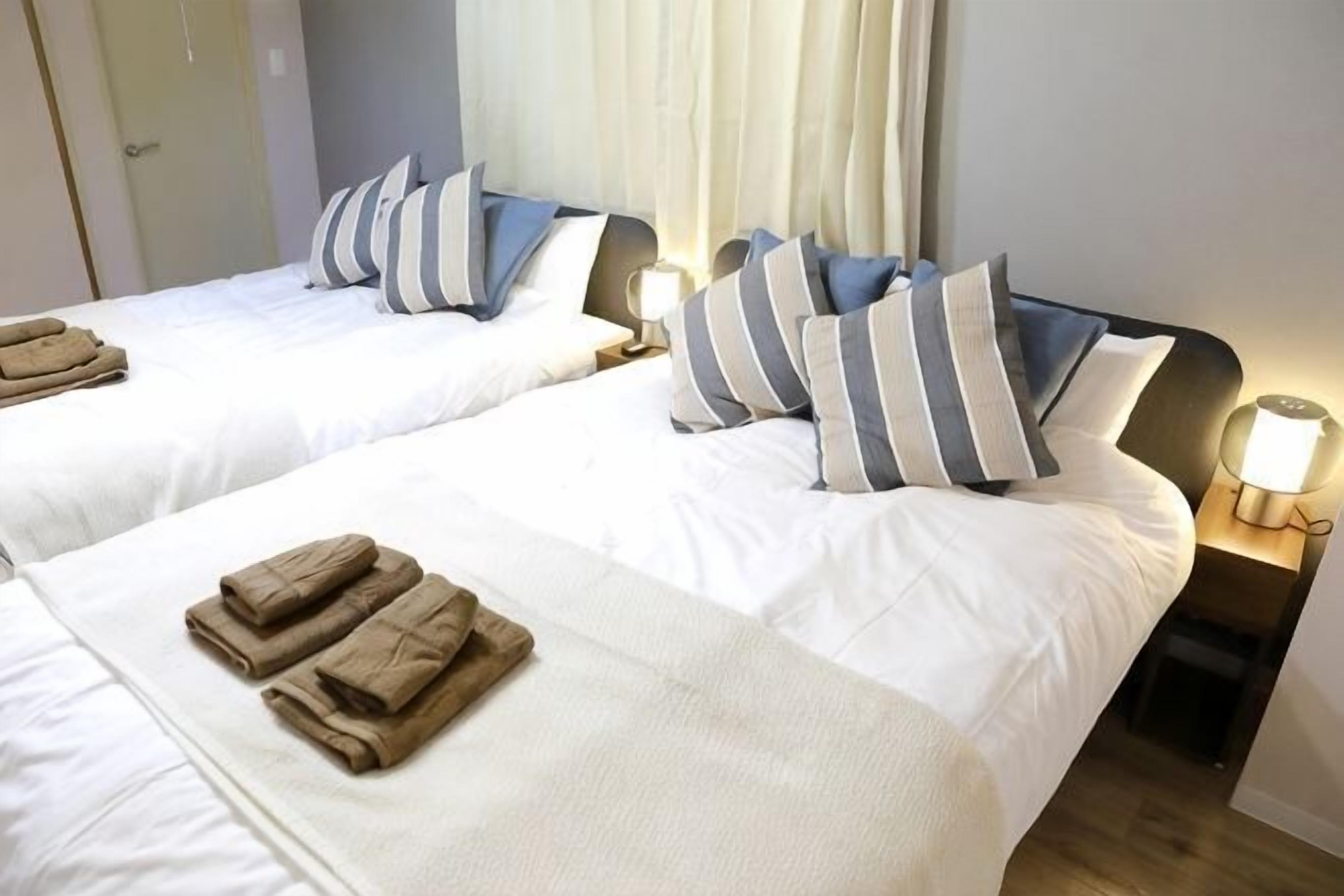Habitación de hotel con dos camas, cada una con almohadas y una lámpara de noche.