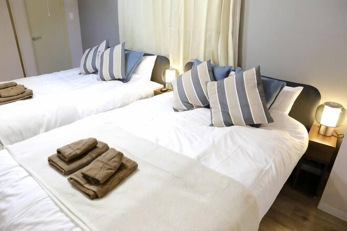 A hotel room with two beds, each with pillows and a bedside lamp.