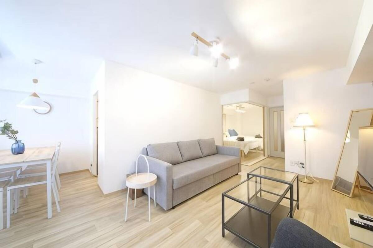 A modern living room with a sofa, a glass coffee table, a dining table with chairs, and a lamp.